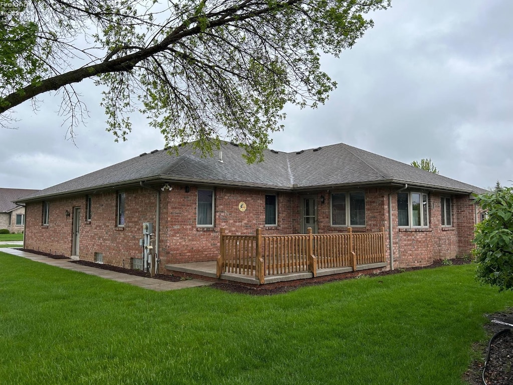 rear view of house featuring a lawn, a wooden deck, a shingled roof, and brick siding