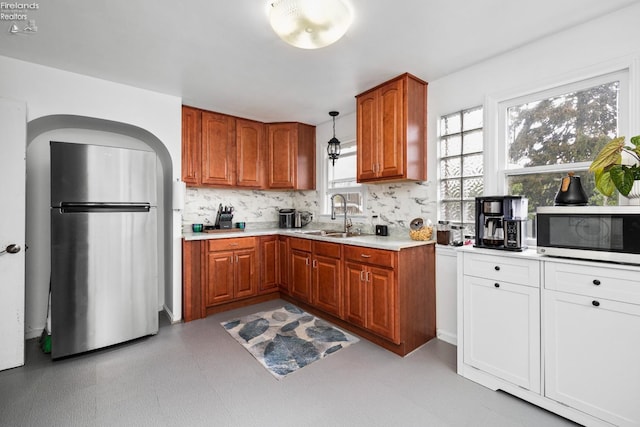 kitchen featuring stainless steel appliances, a sink, backsplash, brown cabinets, and light countertops