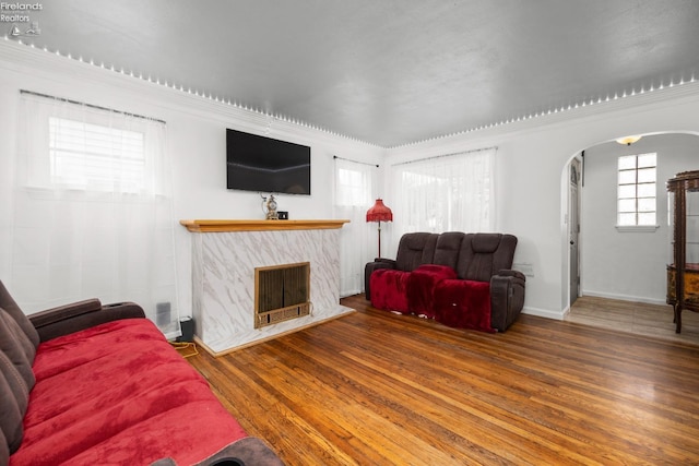living area with a fireplace, arched walkways, baseboards, and wood finished floors