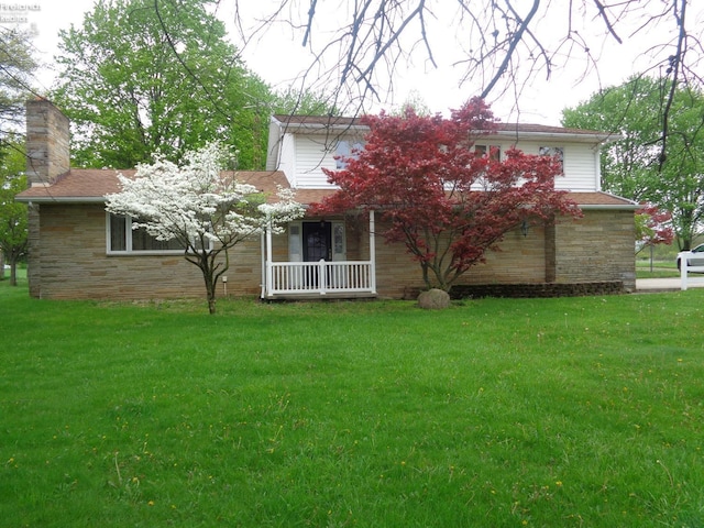 rear view of house with a yard, stone siding, a shingled roof, and a chimney