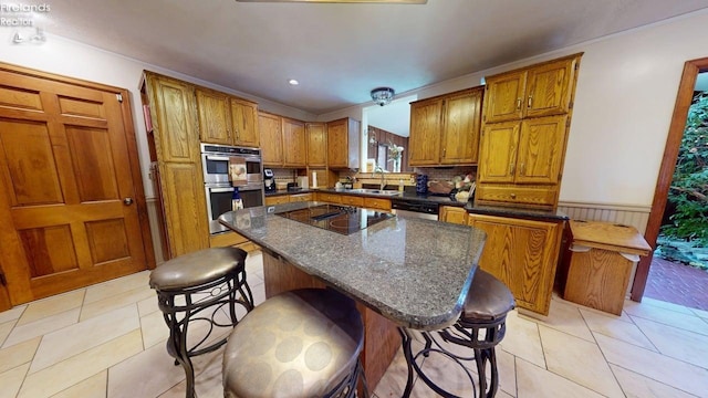 66 Hillcrest Dr, Willard, OH 44890 - kitchen with double oven, brown cabinetry, black electric cooktop, wainscoting, and a kitchen bar