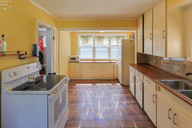 kitchen featuring white appliances, a sink, crown molding, dark wood finished floors, and tasteful backsplash