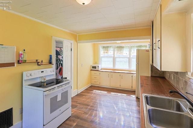 kitchen with white appliances, a sink, crown molding, dark wood-style flooring, and tasteful backsplash