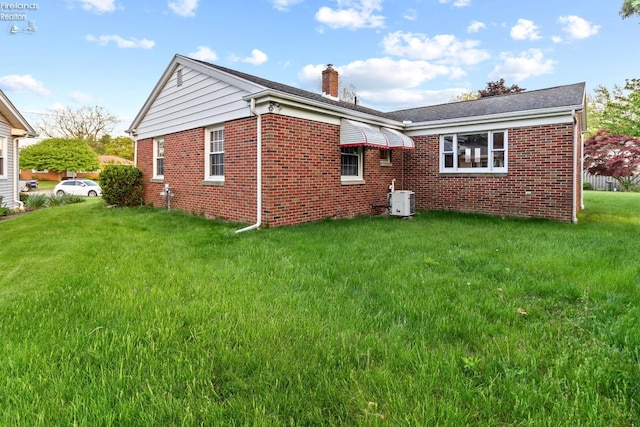 rear view of house featuring a chimney, brick siding, and a yard
