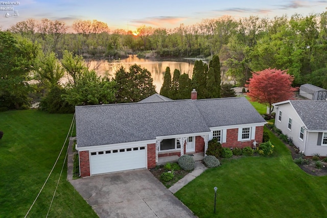 view of front of home featuring brick siding, a garage, driveway, a water view, and a lawn