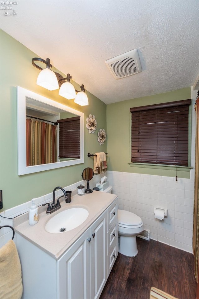 bathroom featuring tile walls, toilet, vanity, wood finished floors, and a wainscoted wall