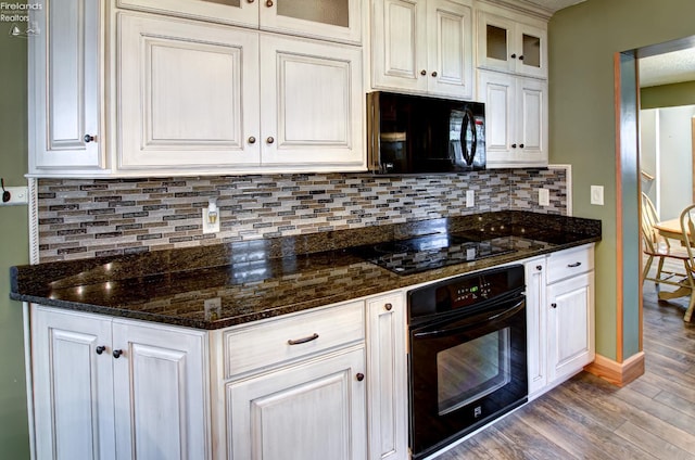 5475 E Mabel Dr, Port Clinton, OH 43452 - kitchen featuring black appliances, wood finished floors, glass insert cabinets, decorative backsplash, and dark stone counters
