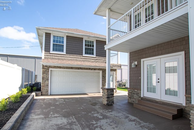 5475 E Mabel Dr, Port Clinton, OH 43452 - view of exterior entry with french doors, concrete driveway, a balcony, an attached garage, and stone siding