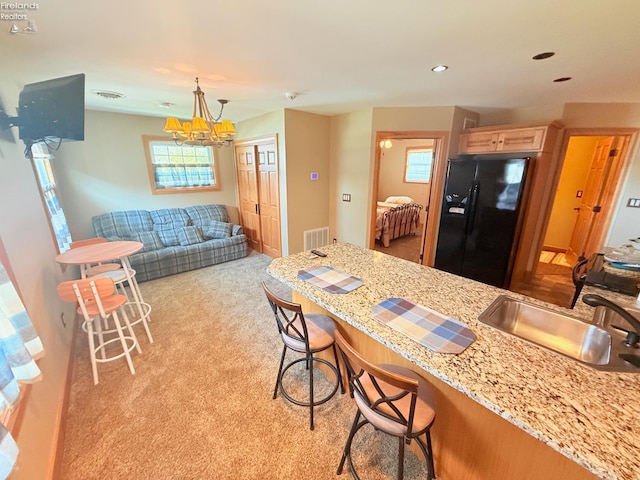 5475 E Mabel Dr, Port Clinton, OH 43452 - kitchen with black fridge, a sink, light carpet, a breakfast bar area, and a chandelier