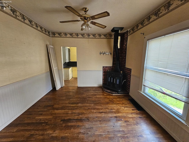 202 Duane St, Clyde, OH 43410 - unfurnished living room featuring a wood stove, wood finished floors, a ceiling fan, and wainscoting