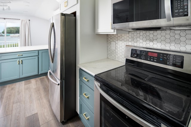 6039 E Harbor Rd Unit 8, Marblehead, OH 43440 - kitchen with appliances with stainless steel finishes, blue cabinets, vaulted ceiling, wood finished floors, and backsplash