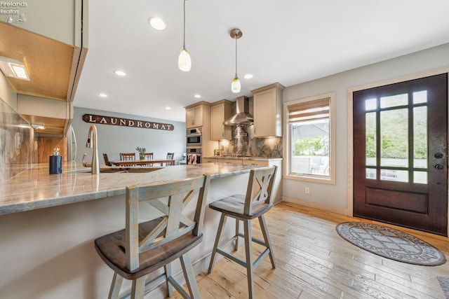 3999 NE Catawba Rd Unit 29, Port Clinton, OH 43452 - kitchen with wall chimney range hood, a kitchen bar, tasteful backsplash, a peninsula, and light stone counters