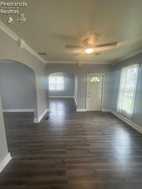 201 Heter St, Bellevue, OH 44811 - unfurnished dining area with baseboards, crown molding, arched walkways, ceiling fan, and dark wood-style flooring