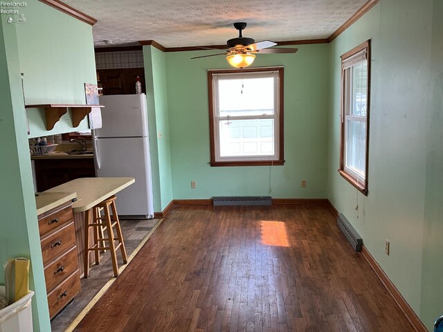 52 Prospect St, New London, OH 44851 - unfurnished dining area with crown molding, dark wood finished floors, ceiling fan, a baseboard heating unit, and a textured ceiling