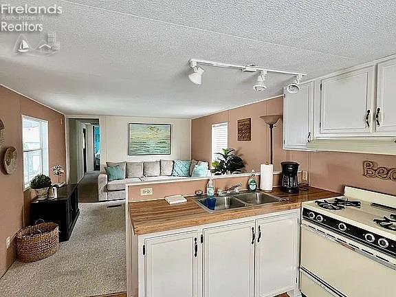3575 NE Catawba Rd Unit 5, Port Clinton, OH 43452 - kitchen with white range with gas stovetop, a sink, a peninsula, white cabinets, and a textured ceiling