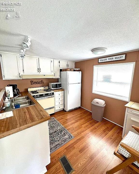 3575 NE Catawba Rd Unit 5, Port Clinton, OH 43452 - kitchen with white appliances, white cabinetry, a textured ceiling, a sink, and wood finished floors