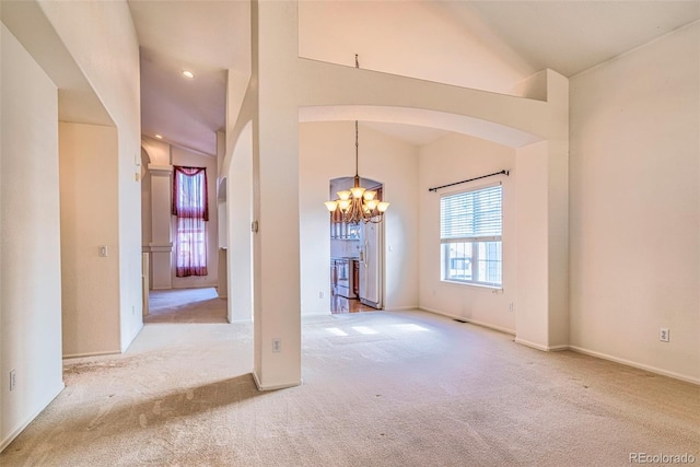 empty room with light colored carpet, high vaulted ceiling, and a notable chandelier