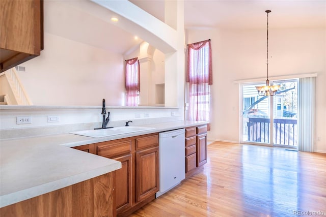 kitchen featuring sink, white dishwasher, light hardwood / wood-style flooring, pendant lighting, and vaulted ceiling