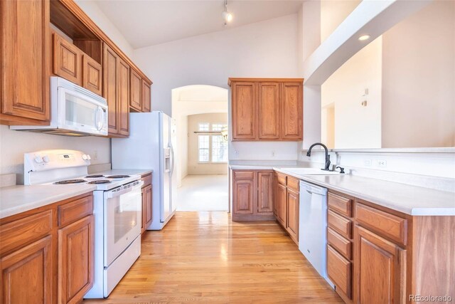 kitchen featuring light wood-type flooring, lofted ceiling, sink, and white appliances