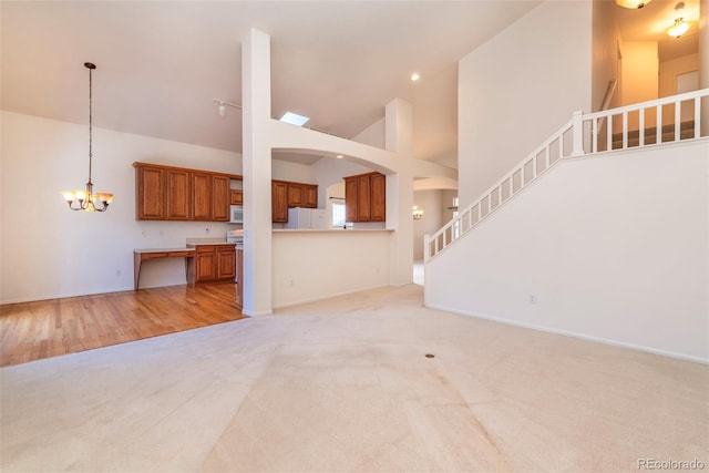 unfurnished living room with high vaulted ceiling, light wood-type flooring, and a chandelier