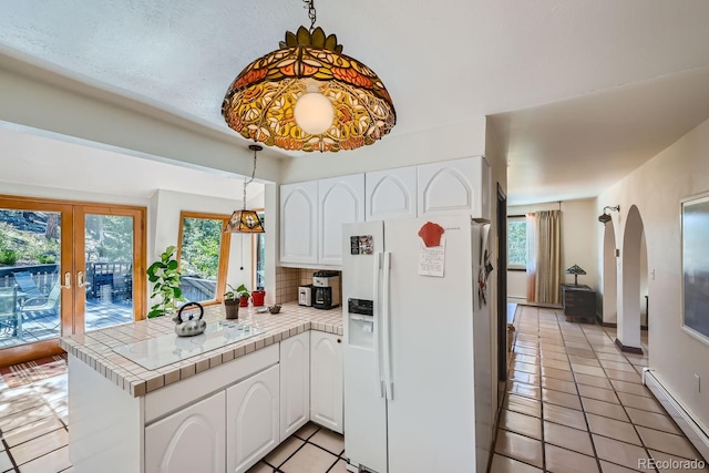 kitchen featuring white fridge with ice dispenser, white cabinetry, kitchen peninsula, a baseboard radiator, and decorative light fixtures