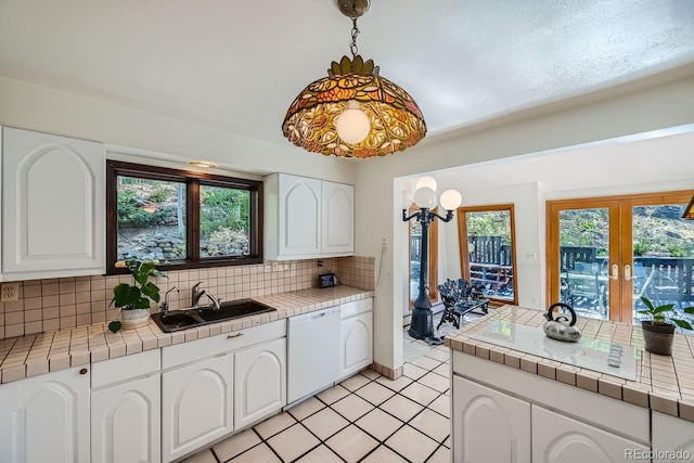 kitchen featuring a healthy amount of sunlight, tile counters, white dishwasher, and tasteful backsplash