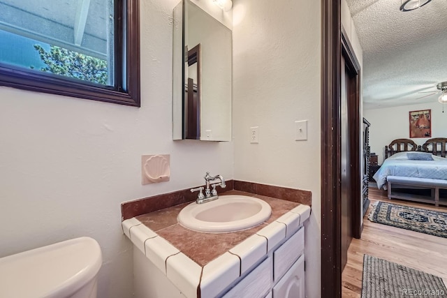 bathroom featuring vanity, a textured ceiling, wood-type flooring, ceiling fan, and toilet