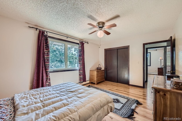 bedroom with a baseboard heating unit, a closet, a textured ceiling, light hardwood / wood-style flooring, and ceiling fan