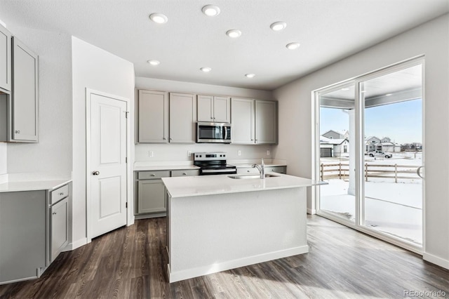 kitchen featuring sink, appliances with stainless steel finishes, gray cabinetry, dark hardwood / wood-style floors, and a center island with sink