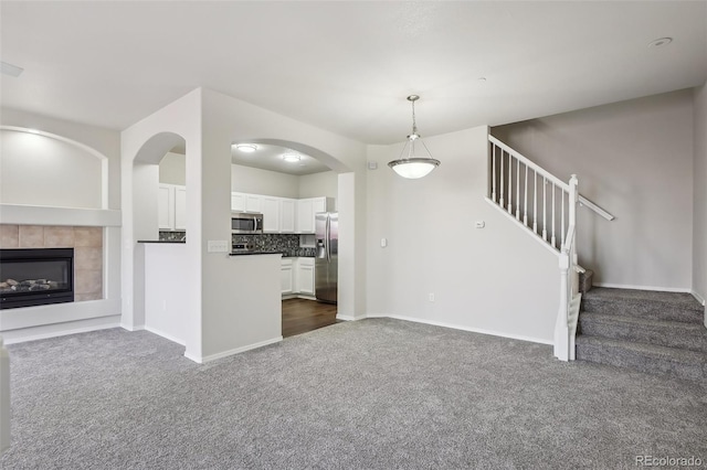 unfurnished living room featuring stairs, baseboards, a fireplace, and dark colored carpet