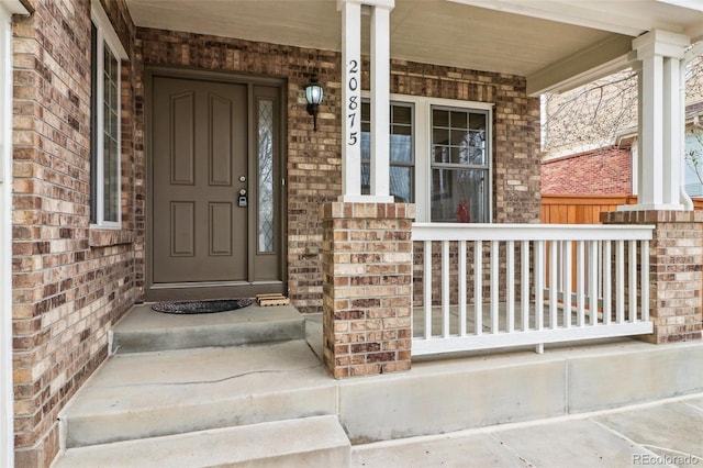 view of exterior entry featuring a porch and brick siding
