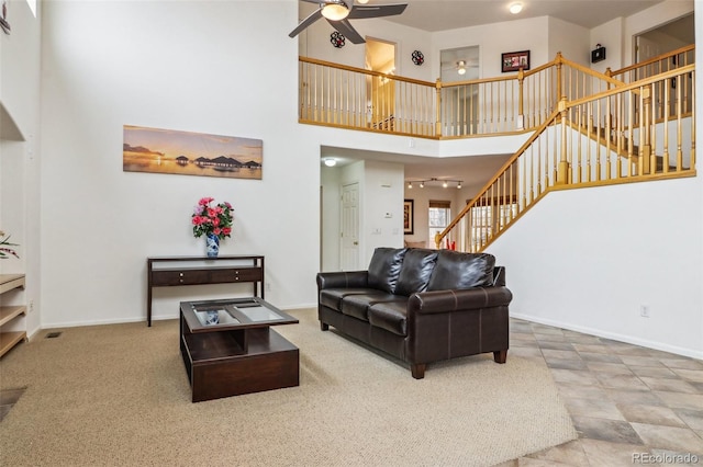 living room featuring stairs, a towering ceiling, baseboards, and a ceiling fan