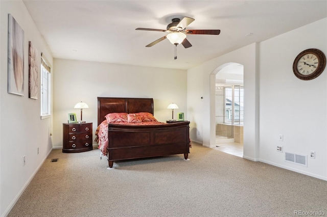 carpeted bedroom with visible vents, baseboards, arched walkways, a ceiling fan, and ensuite bath