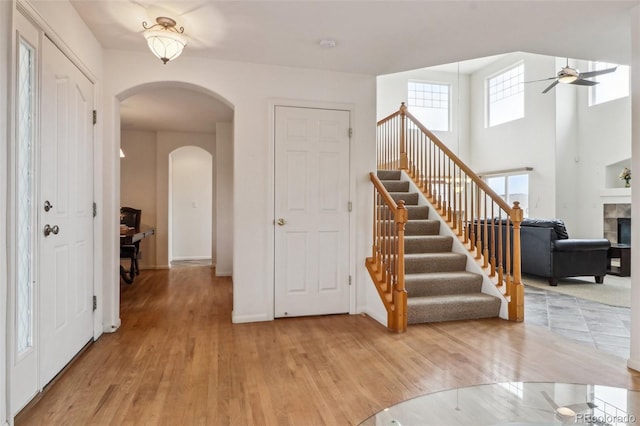 entrance foyer with light wood finished floors, stairway, arched walkways, and a ceiling fan