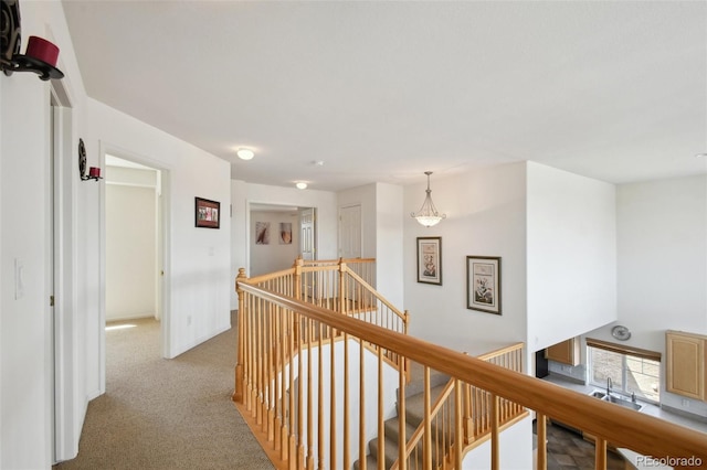 hallway featuring carpet floors, baseboards, and an upstairs landing