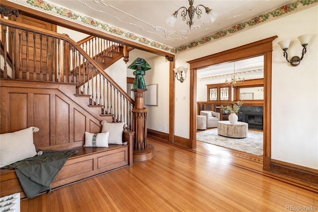 interior space with baseboards, a chandelier, stairs, light wood-style flooring, and a glass covered fireplace