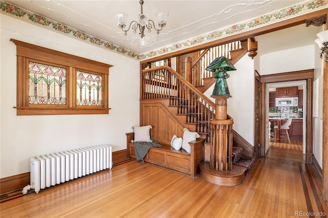 stairs with radiator heating unit, a notable chandelier, baseboards, and hardwood / wood-style flooring