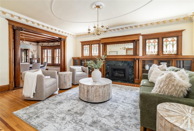living area with a high end fireplace, a notable chandelier, ornamental molding, and wood finished floors