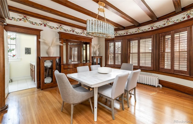 dining room featuring light wood-style floors, radiator heating unit, a chandelier, baseboards, and beam ceiling