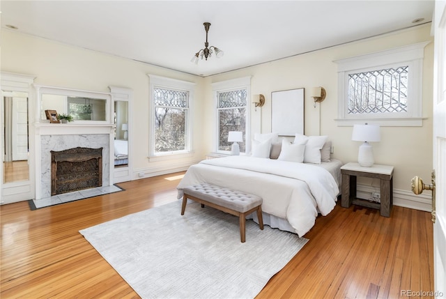 bedroom with wood finished floors, an inviting chandelier, a high end fireplace, and multiple windows