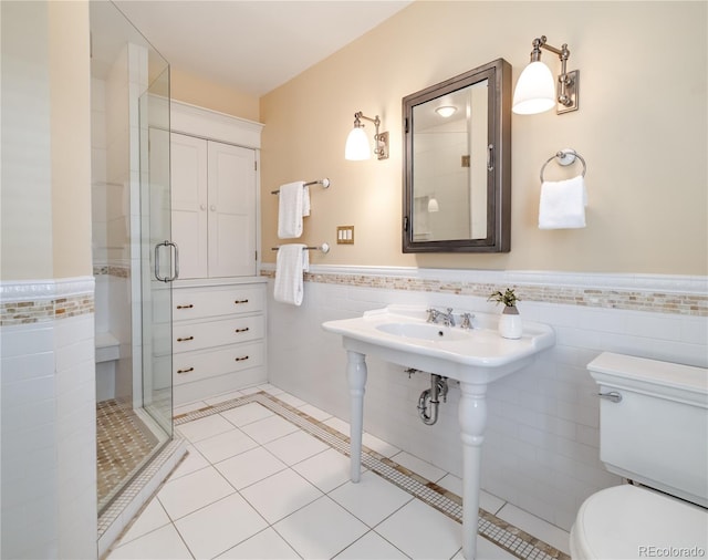 bathroom featuring a stall shower, tile patterned floors, toilet, a wainscoted wall, and tile walls