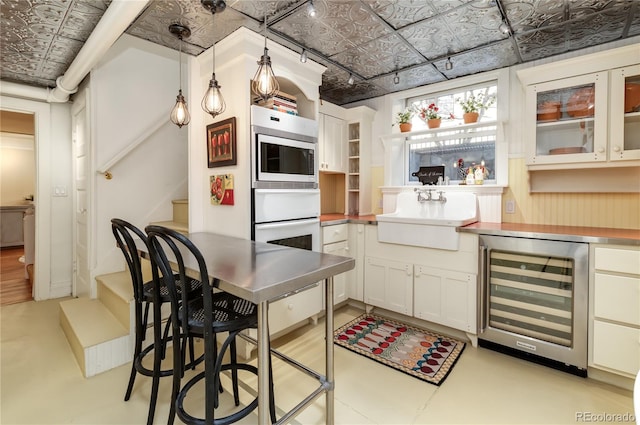 kitchen with glass insert cabinets, a sink, beverage cooler, and an ornate ceiling