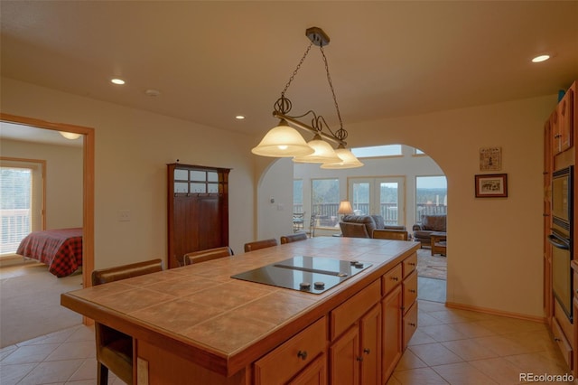 kitchen featuring light tile floors, a kitchen bar, black electric cooktop, decorative light fixtures, and tile counters