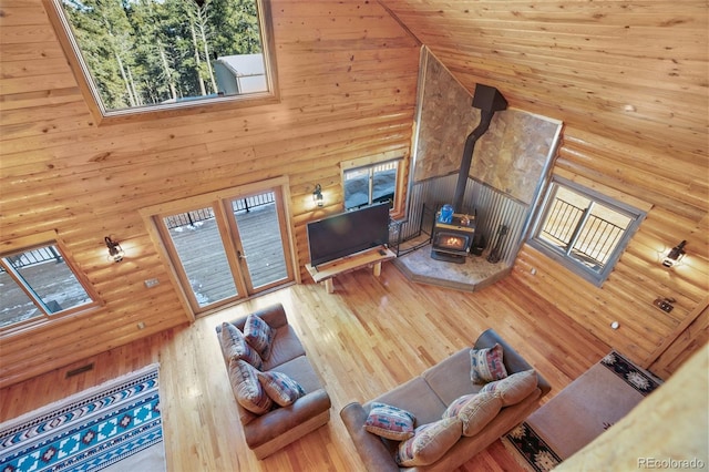 living room featuring a wood stove, wood walls, high vaulted ceiling, and hardwood / wood-style flooring