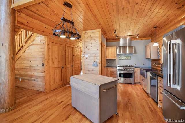 kitchen with light brown cabinetry, high end appliances, wall chimney range hood, light hardwood / wood-style flooring, and hanging light fixtures