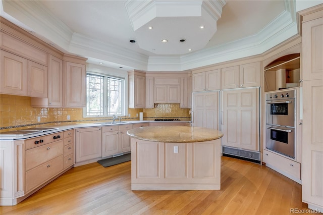 kitchen with light wood finished floors, stainless steel double oven, a kitchen island, and ornamental molding