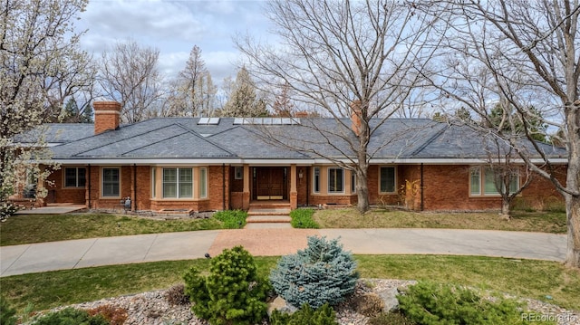 ranch-style home with a chimney, brick siding, and a front yard