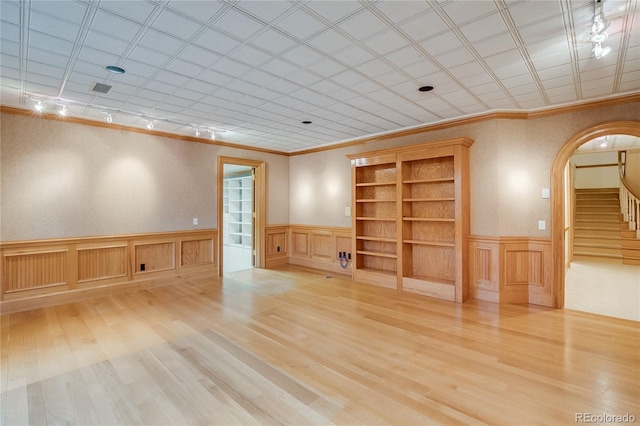 spare room featuring arched walkways, wood finished floors, ornamental molding, and wainscoting