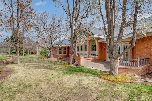 rear view of property with brick siding, a yard, and a patio area