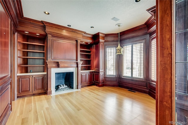 unfurnished living room featuring a fireplace with flush hearth, crown molding, visible vents, and light wood-style flooring